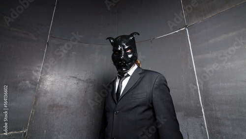 Canvas Print A corporate man in a dirty scruffy suit wearing a black pigs mask in a dark sinister background, photographed with moody cinematic lighting