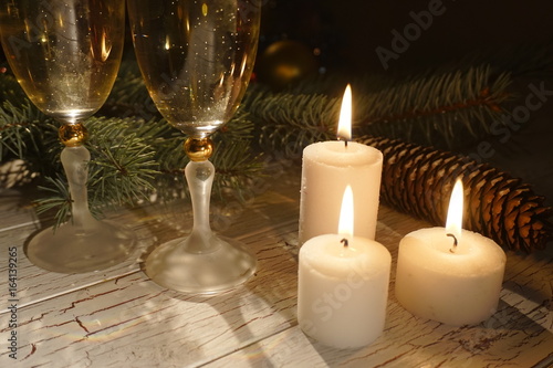 Romantic New Year composition of the three glowing candles near the glasses of champahne at the background of the cones. photo