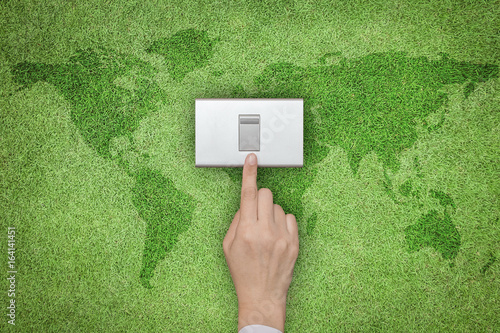 Energy saving and ecological friendly concept with hand turning off switch on green grass lawn with world map photo