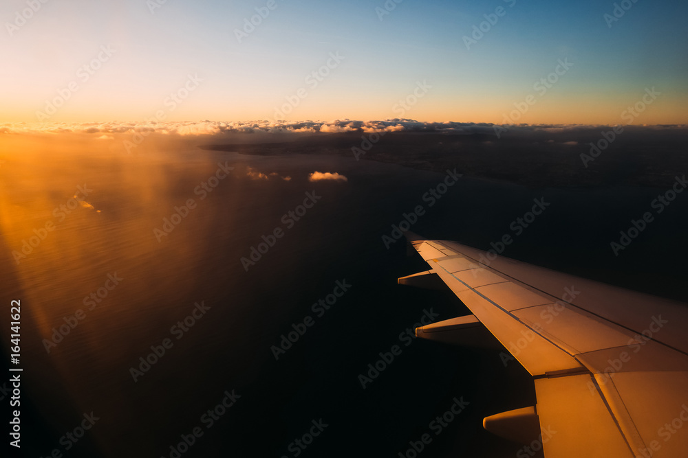 View from airplane window above Portugal at sunset. Sun shining from the corner of image on the aircraft wing with large water space beneath