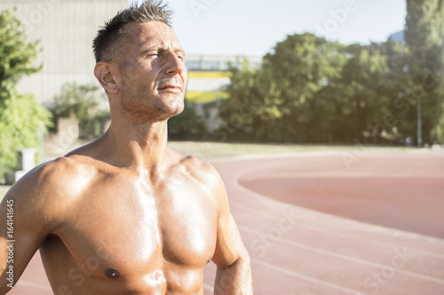 Handsome middle aged man working out on a running track. Healthy adult man sun baiting. Tanned skin and shirtless middle-aged man.