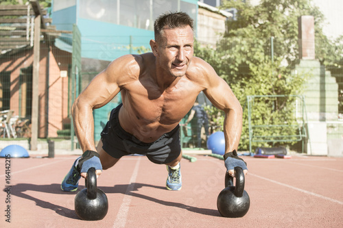 Crossfit training. Fitness man doing a weight training by lifting kettlebell. Midleaged athlete doing kettlebell push ups. Bodybuilder lifting kettlebell. Crossfit instructor at the track.