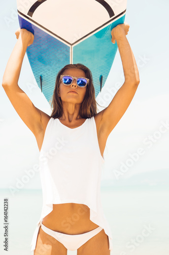 Photography Sexy slim lady in sensual tunica and sunglasses on a tropical beach hold her surfboard over herself