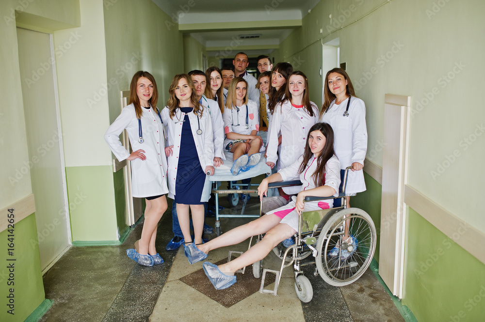 Crazy young doctors having fun by posing on a wheelchair in the hallway of hospital.