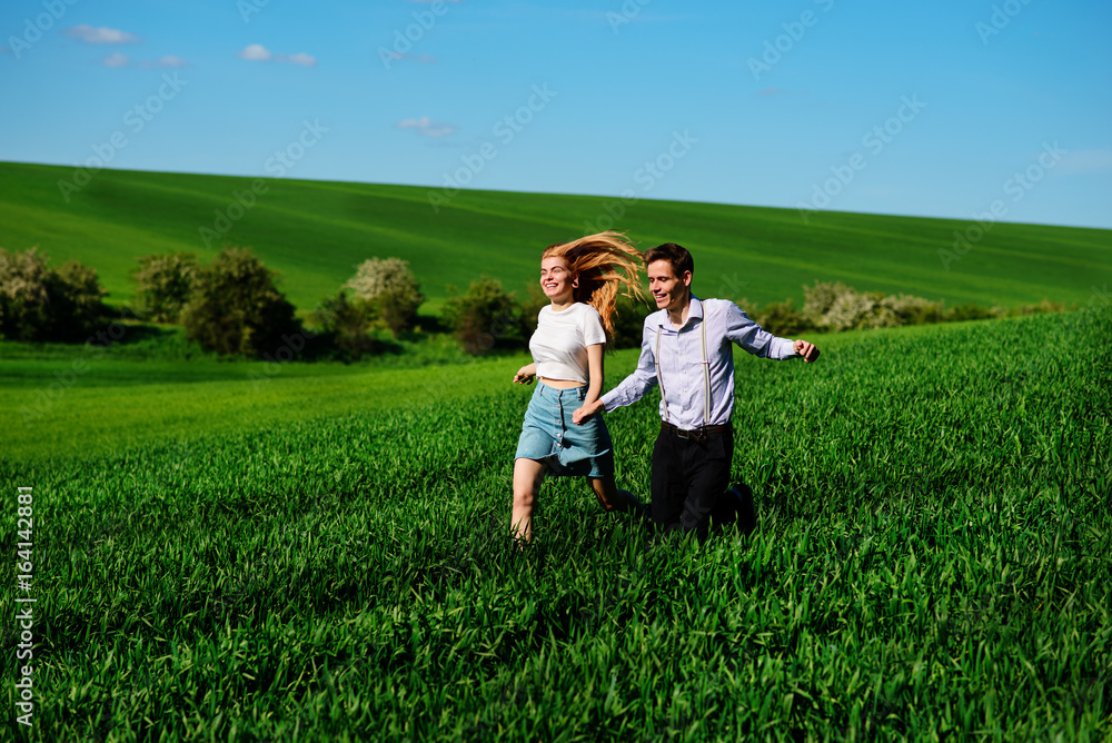 Young happy lovers running on meadow with green grass and blue sky Young happy lovers running on meadow with green grass and blue sky