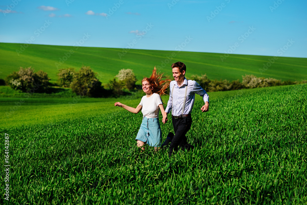 Young happy lovers running on meadow with green grass and blue sky Young happy lovers running on meadow with green grass and blue sky