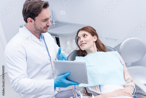 portrait of dentist pointing at tablet while discussing treatment with patient