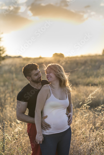 Young couple posing in sunset. Pregnant woman and her husband in nature.