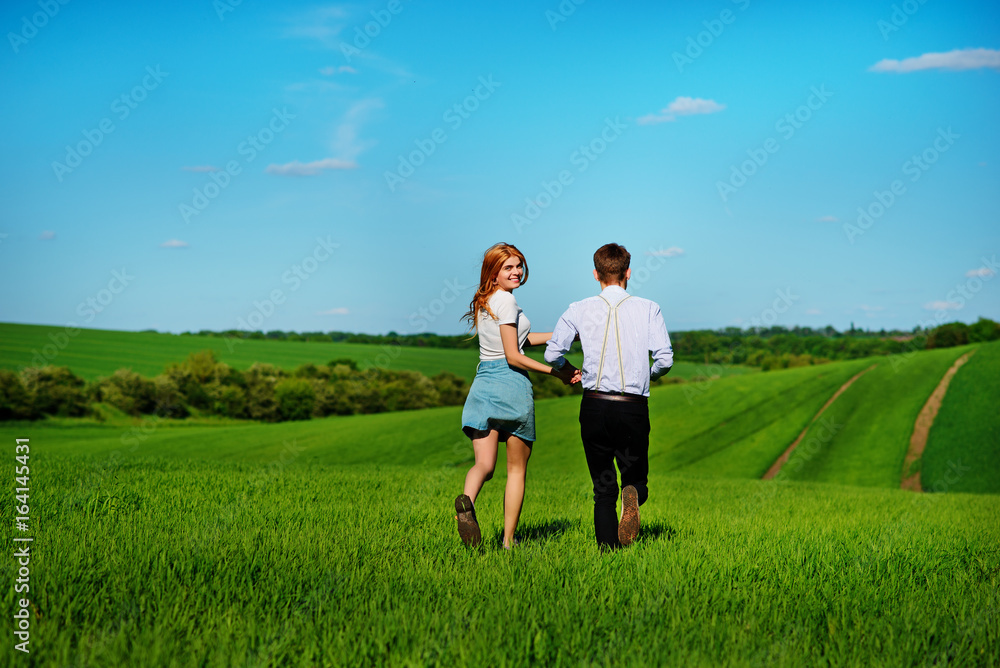 Young couple running along a green field on a lovely sunny day