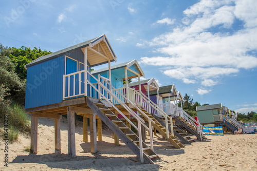 Rows of colourful wooden beach huts on a sandy beach in Norfolk, UK under a blue sky and summer sunshine. © teamjackson