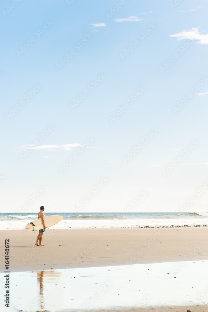 Handsome boy in blue swimming shorts and cap walk with long surf surfing board wait on surf spot at sea ocean beach. White blank surfboard. Concept of power, freedom, new modern life, generation Y.