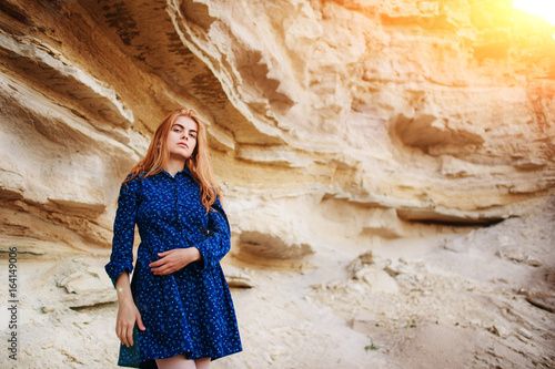 Beautiful redheaded girl standing in a blue dress in the middle of a sand quarry