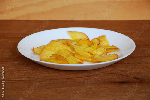 Dried and fried cassava slices place on white plate isolated on wood texture background. This is local Malaysian traditional junk food call Kerepek Ubi.  