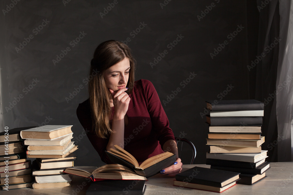 the girl sitting at the table reading a lot of books the girl sitting at the table reading a lot of books