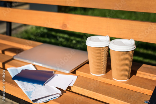 Close-up view of laptop, passports with tickets, map and disposable coffee cups on wooden bench