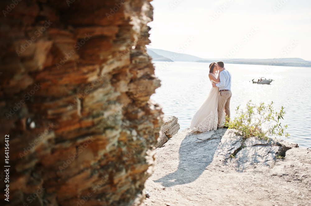 Newly married couple dancing on the rocky cliff with a view of a lake in the background on their wedding day.