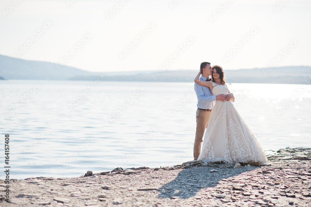 Amazing young couple holding hands on the lake shore on their sunny wedding day. Amazing young couple holding hands on the lake shore on their sunny wedding day.
