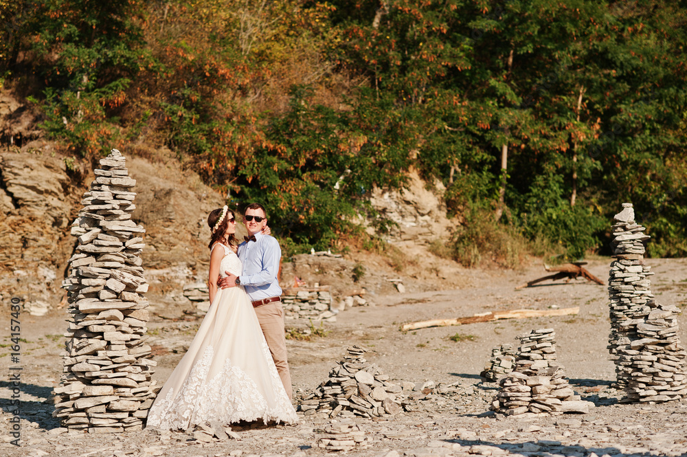 Gorgeous wedding couple standing next to the pile of stones on the lake shore. Gorgeous wedding couple standing next to the pile of stones on the lake shore.