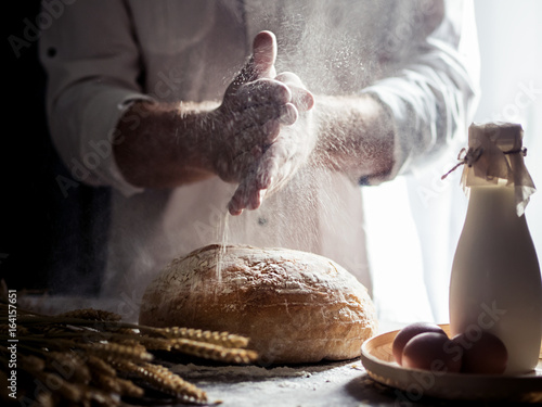 Man sprinkling flour over freshly baked bread on kitchen table