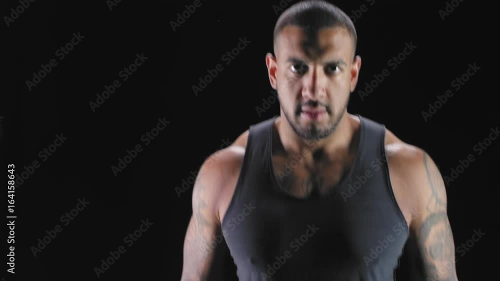 Portrait shot of a muscular black man jumping around, and staring at the camera on a dark background. Portrait shot of a muscular black man jumping around, and staring at the camera on a dark background.