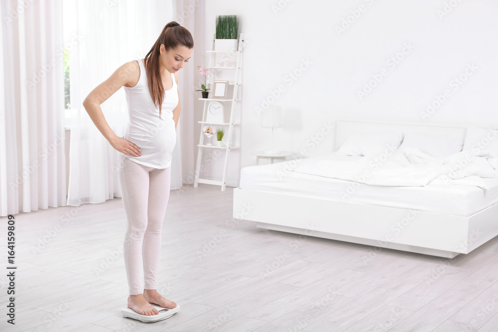 Pregnant woman standing on scales at home. Pregnancy weight gain concept