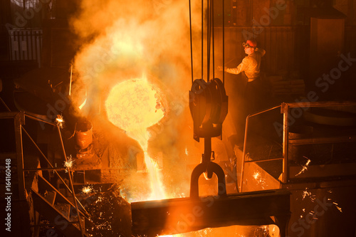 Working in a foundry. Worker looking down, red color is a reflection of the molten metal. Very high heat and purple fringing. See more images and video from this series.