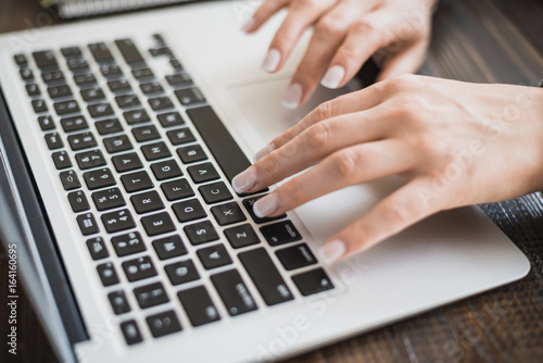 Work of a business lady. Female hands working on a modern laptop. On a wooden table. Horizontal frame