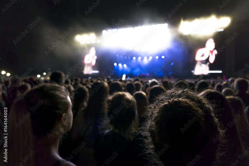 silhouettes of concert crowd in front of bright stage lights. Dark background, smoke, concert spotlights