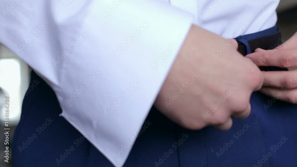 Man tightens the black leather belt on the blue pants, close-up. Man fastens the belt on his trousers, close-up. Man tightens the black leather belt on the blue pants, close-up. Man fastens the belt on his trousers, close-up.