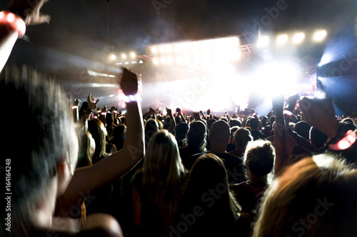 silhouettes of concert crowd in front of bright stage lights. Dark background, smoke, concert spotlights