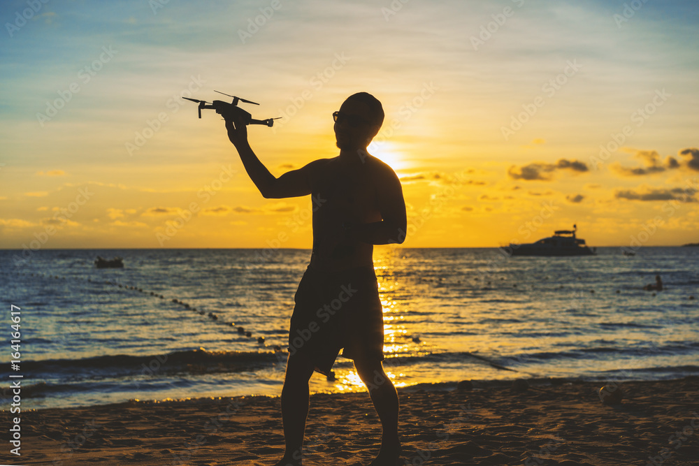 Young man at sunset on the beach with quadrocopter in hand, seascape with copy space