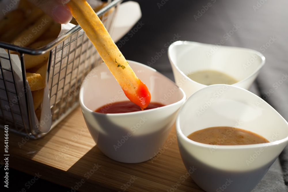 French fries in a metal basket with sauce on a wooden floor.