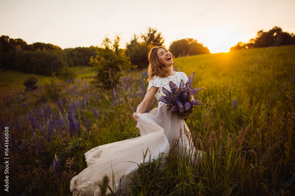 Golden rays of evening sun illuminate gorgeous lady with bouquet on the field