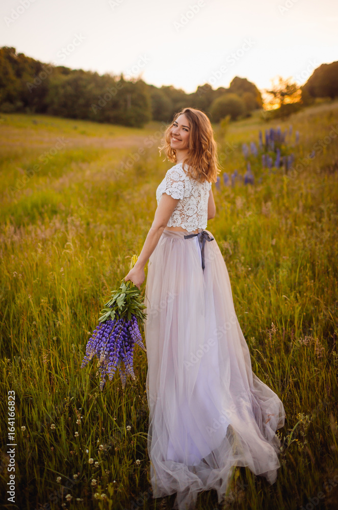 Woman in marvelous dress walks on the field with flowers
