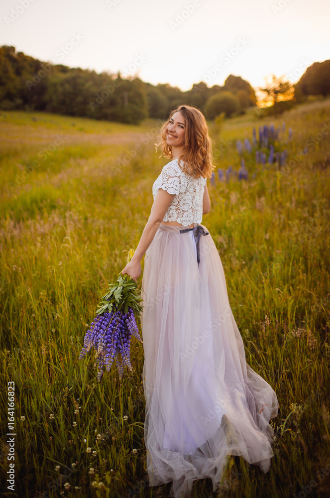 Woman in marvelous dress walks on the field with flowers Woman in marvelous dress walks on the field with flowers
