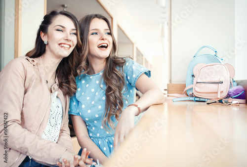 Two happy smiling young beautiful woman having good time in a cafe. Two friends laughing, drinking coctails and making selfie photo