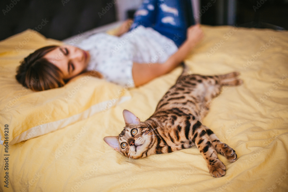 Woman and Bengal cat lie on the bed Woman and Bengal cat lie on the bed