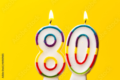 Number 80 birthday celebration candle against a bright yellow background