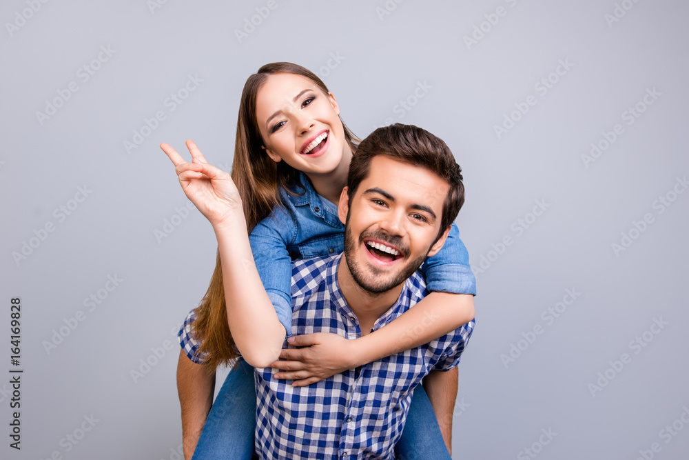 Love forever, fun together. Young brunete handsome bearded boyfriend is piggy backing his cute lover, wearing casual clothes, on pure background Love forever, fun together. Young brunete handsome bearded boyfriend is piggy backing his cute lover, wearing casual clothes, on pure background