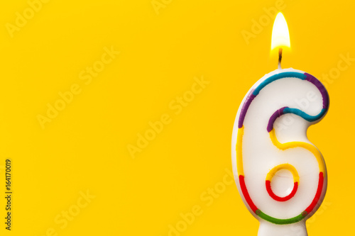 Number 6 birthday celebration candle against a bright yellow background