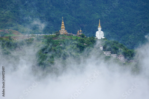 White Buddha Image with pagoda on hill covering with fog