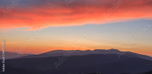 Reddish sunrise with mountains and clouds. Atmospheric phenomena concept