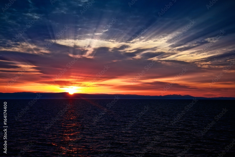 Beautiful sunrise in the ocean. Sun rays between sky clouds. Dramatic picture.
