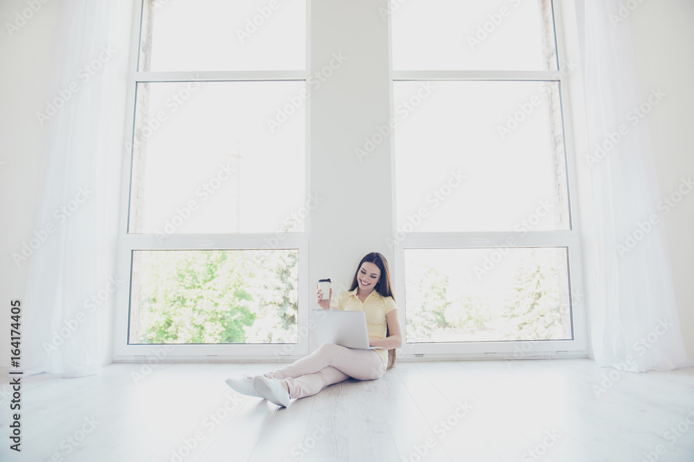 So comfortable and easy! Young happy girl is typing on her laptop sitting on the floor indoors at home, having tea, smiling So comfortable and easy! Young happy girl is typing on her laptop sitting on the floor indoors at home, having tea, smiling