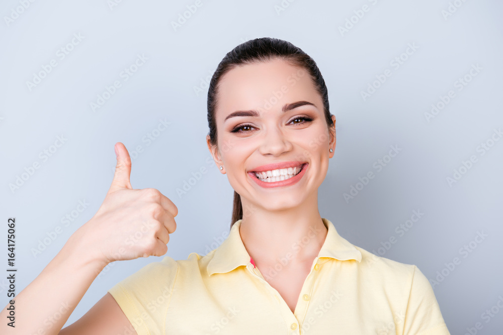 Close up of young gorgeous toothy girl, standing on the pure light blue background and smiling, wearing a yellow tshirt and showing like sign, smiling Close up of young gorgeous toothy girl, standing on the pure light blue background and smiling, wearing a yellow tshirt and showing like sign, smiling