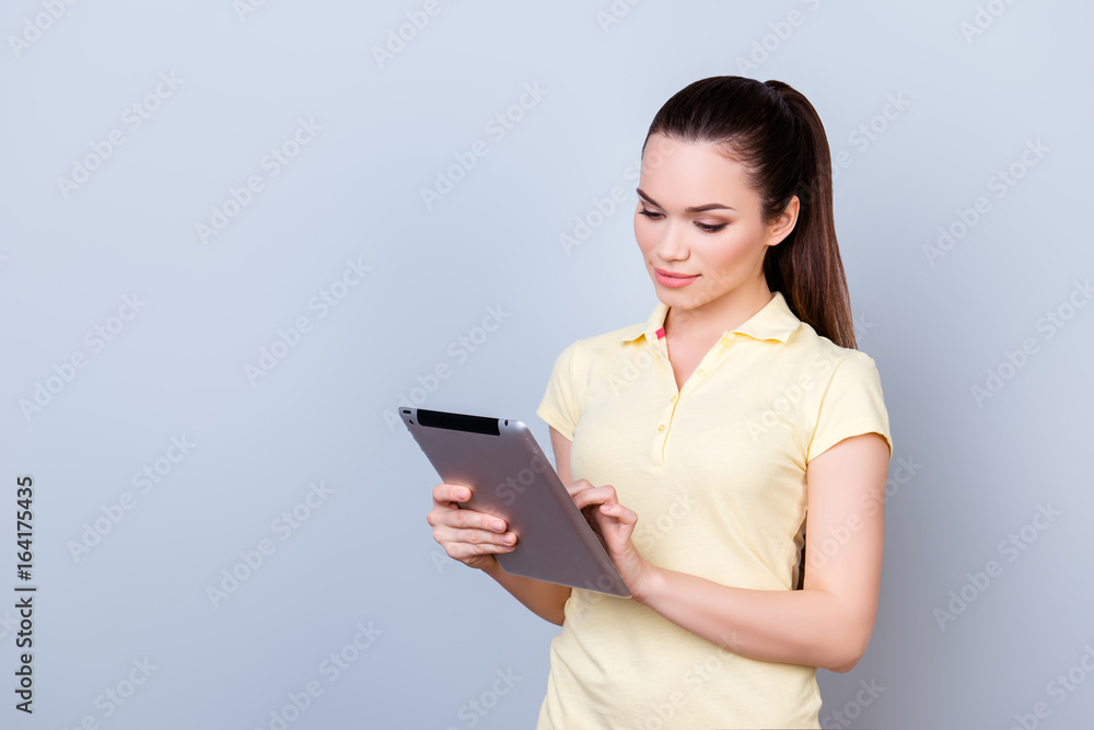 Focused pretty brunette student is typing on her tablet, standing in a yellow tshirt on the pure background. So serious and intelligent Focused pretty brunette student is typing on her tablet, standing in a yellow tshirt on the pure background. So serious and intelligent
