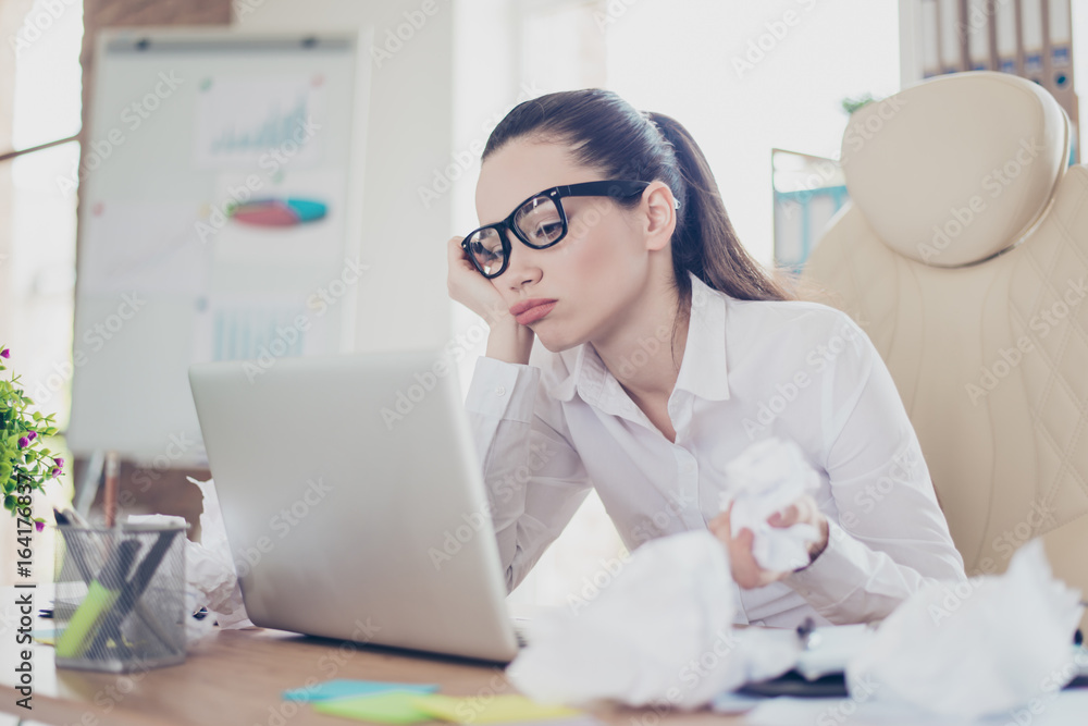 Frustrsted girl which crumpled papers, bored, tired and upset, sitting at the office with pony tail, glasses, in white smart shirt Frustrsted girl which crumpled papers, bored, tired and upset, sitting at the office with pony tail, glasses, in white smart shirt