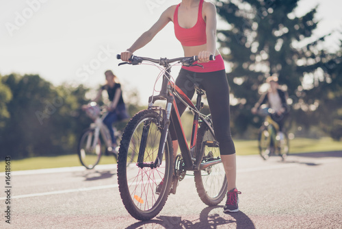 Cropped low angle photo of athletes cycling on the road outdoors, focused on a girl, she stopped, in trandy outfit, sneakers © deagreez