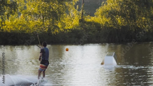 Wakeboarder ride on cable wakeboard in park, outdoor extreme slow motion on water, surfing athlete on water doing boardslide, noseslide or tailslide 180 out