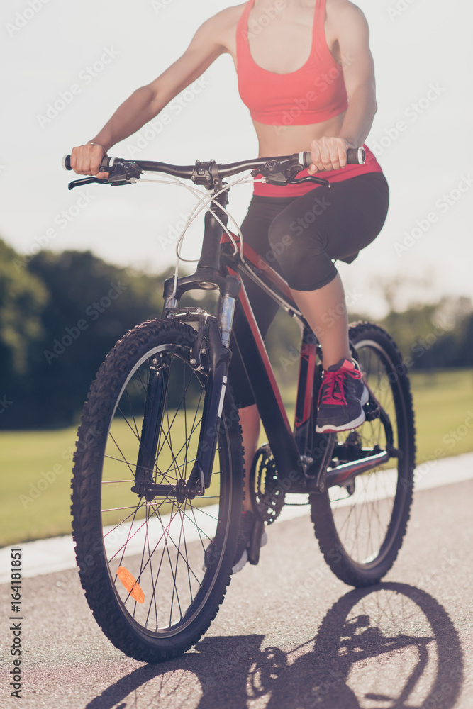 Naklejka premium Cropped low angle photo of female athlete, cycling the modern bike on the track outdoors, in trandy outfit, sneakers